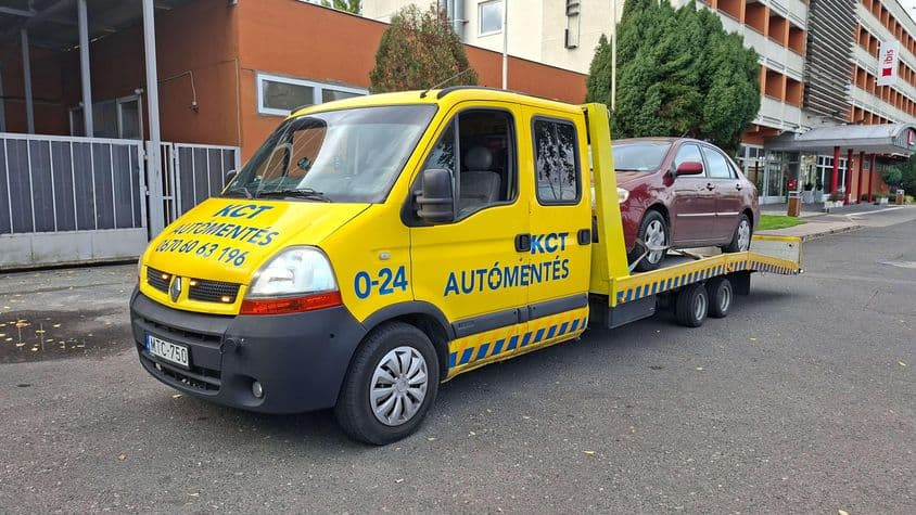 Sárga autómentő szállít piros autót.