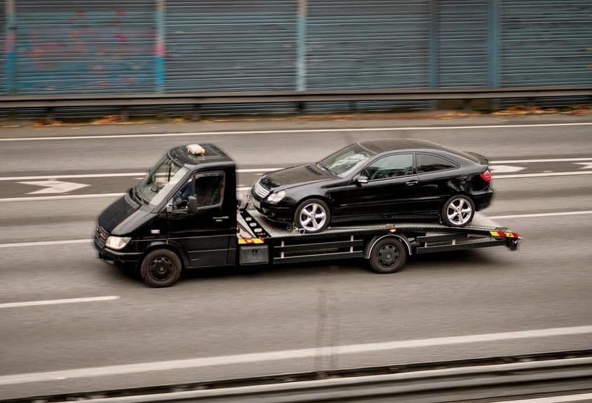 Fekete vontatót szállít régi német kupé autópályán.