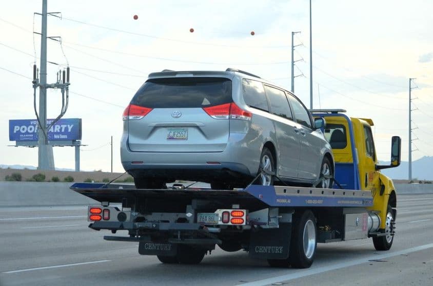 Platós vontató Toyota kisbuszt szállít.