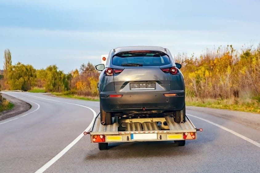 Egy szállító törött sérült autót visz.