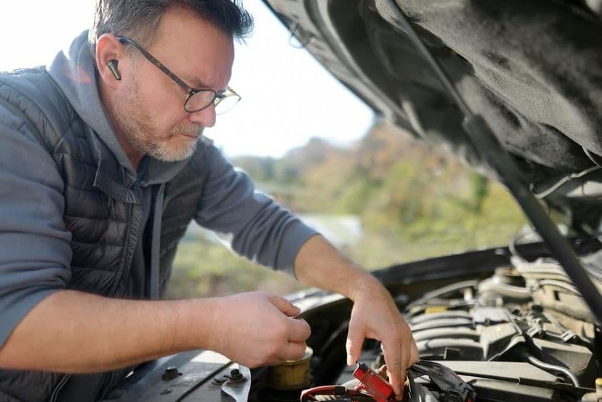 Egy középkorú férfi autót javít utazás közben.