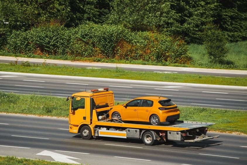 Autómentő járművel sárga autó szállítása.