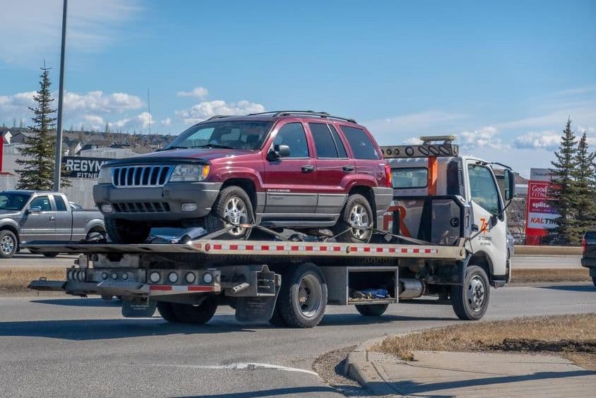 Egy vontató platós teherautó Jeep Grand Cherokee szállít